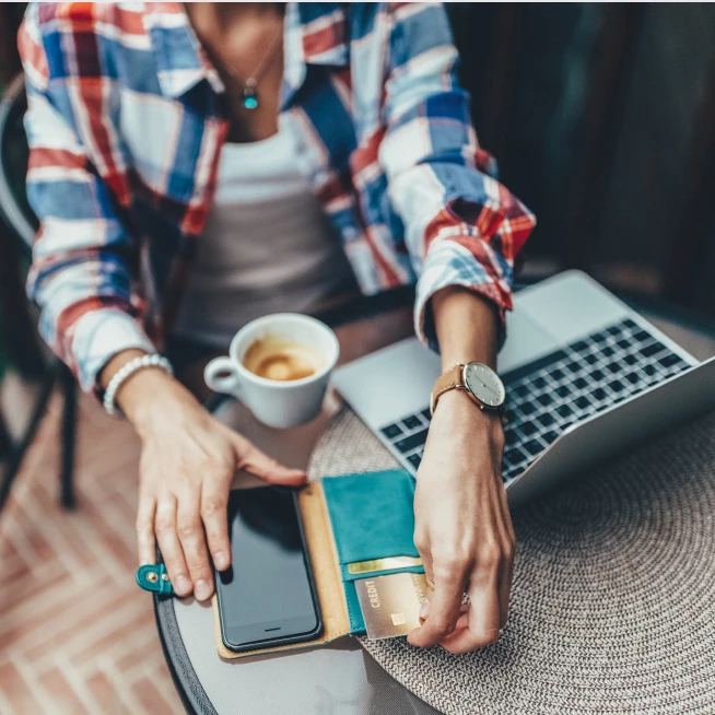 A woman sits in front of the laptop, checking cards in her wallet, and enjoying coffee.