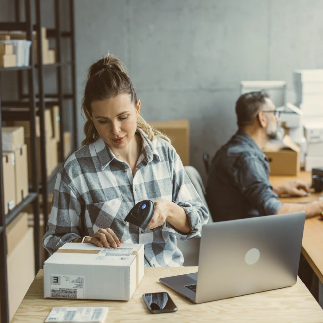 Man on a computer and woman scanning a box in a packing warehouse using Brightspeed business internet.