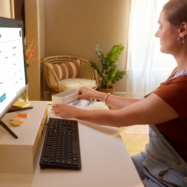 A young lady sitting in front of desktop and checking notes for business solutions.