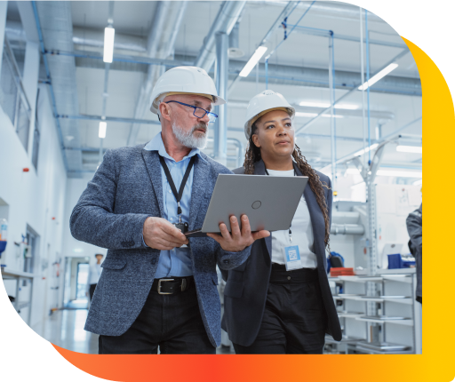  Two professionals review a document on a laptop in a factory.