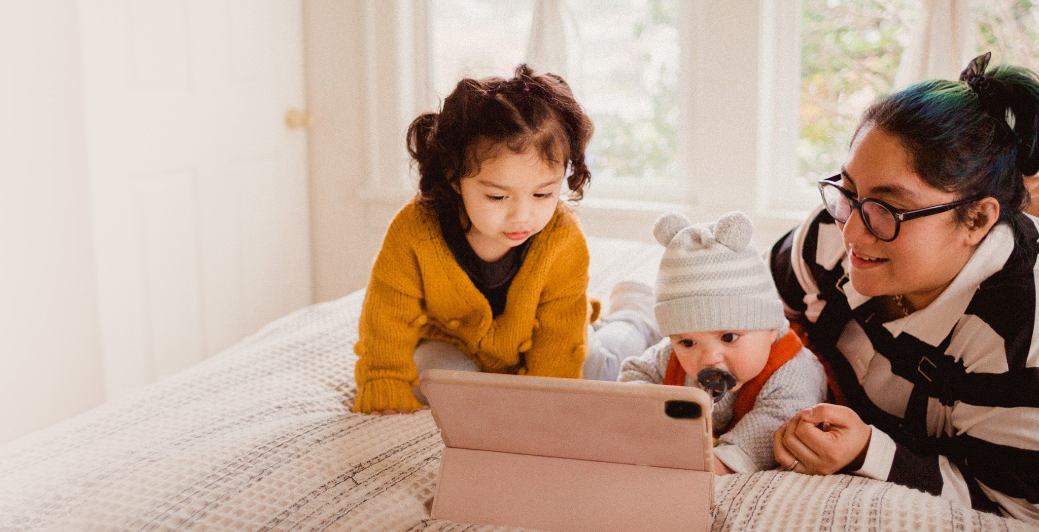 A woman with her two small children looking at a tablet.