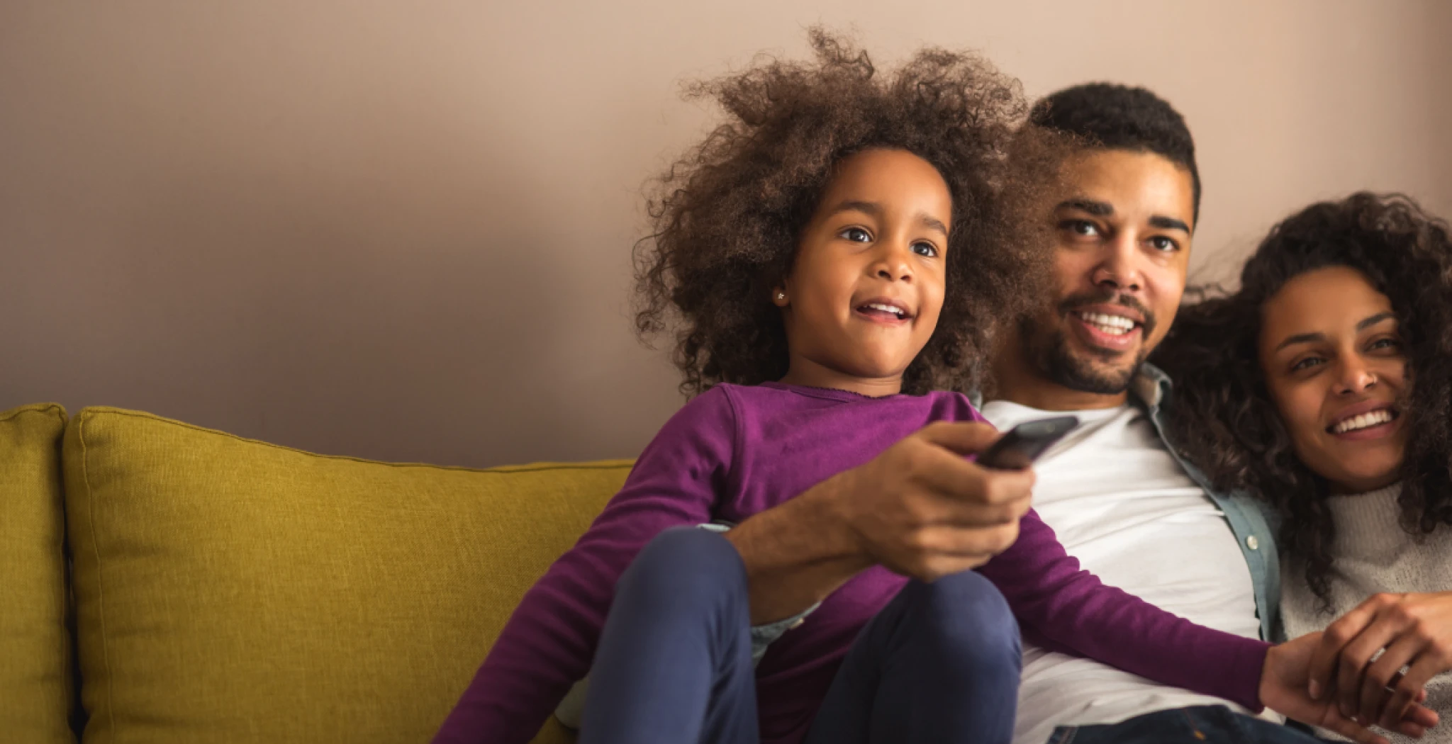 A young couple and a child sitting together on the couch streaming and watching tv