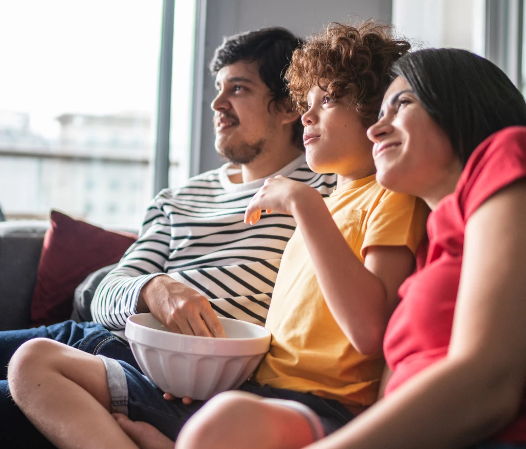 young couple and a child sitting on the couch streaming and watching tv while eating popcorn 