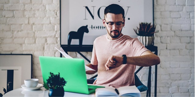 Man checks his watch while he uses his computer