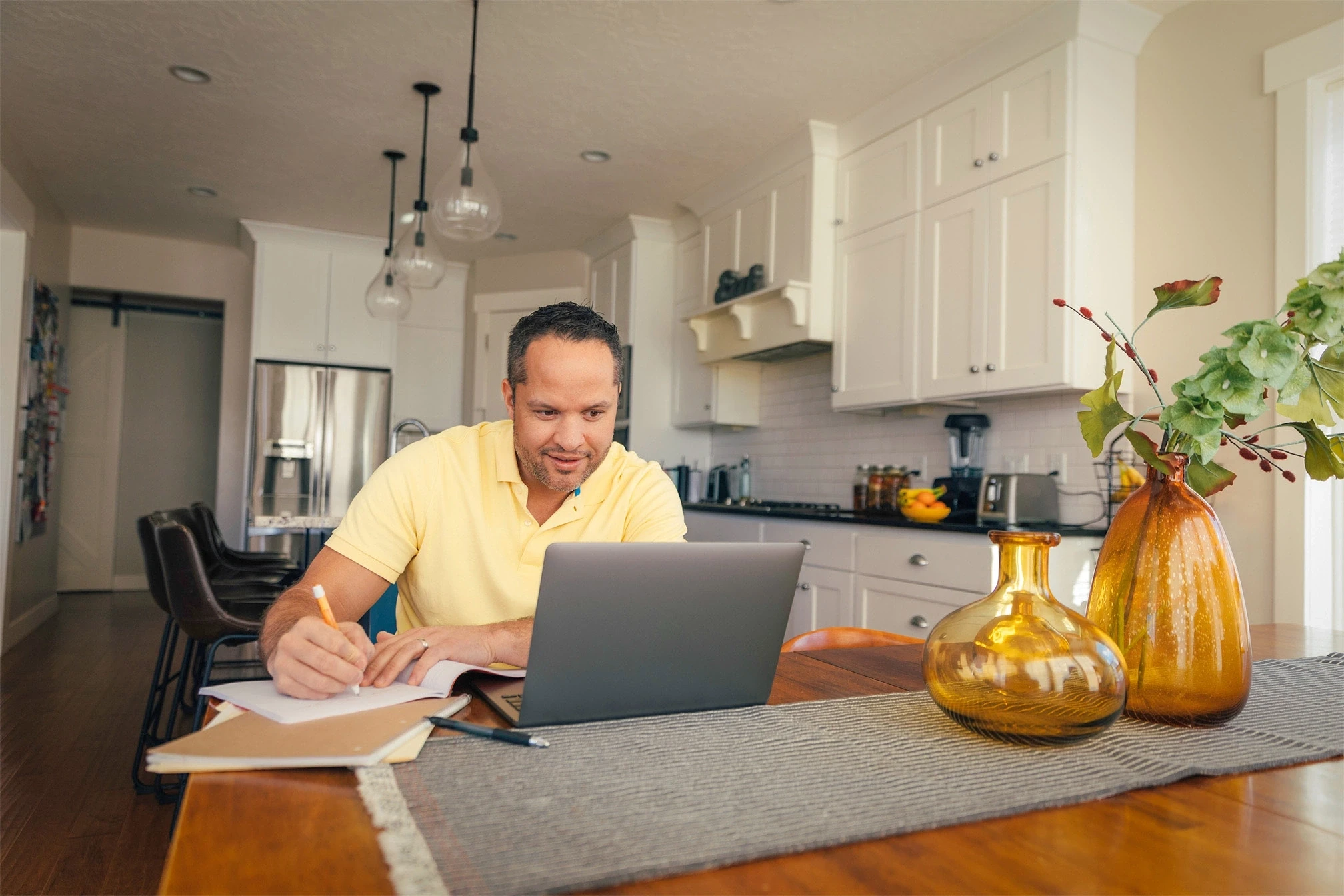 A man multi-tasking while looking at a laptop in a kitchen.